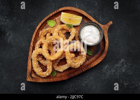 Anelli di calamari di antipasto con salsa su un asse di legno, su cemento grigio. Orizzontale Foto Stock