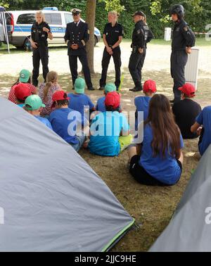 Malchow, Germania. 25th luglio 2022. Varie uniformi di polizia sono presentate ai bambini durante la giornata di azione della polizia e dei vigili del fuoco al campo all'aperto della polizia di Stato di Meclemburgo-Pomerania occidentale 2022. 68 bambini, di cui 15 provenienti dall'Ucraina, partecipano al campo di vacanza della durata di una settimana presso la Scuola Statale di protezione contro incendi e disastri del Meclemburgo-Pomerania occidentale. Il campo libero è destinato a bambini tra i 11 e i 13 anni provenienti da famiglie socialmente svantaggiate. Credit: Bernd Wüstneck/dpa/Alamy Live News Foto Stock