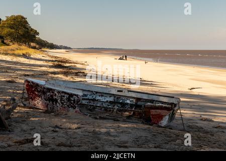 Un vecchio, rotto, piccolo pescatore barca si trova sulla spiaggia in Kiyu, Uruguay. Alcuni pescatori possono essere visti sullo sfondo dell'immagine Foto Stock