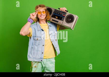 Ritratto di attraente ragazzo allegro hippie tenendo nastro player buon umore riposo isolato su sfondo verde brillante Foto Stock