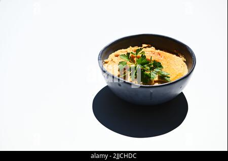 Prezzemolo e ciotola con hummus di ceci sormontato, scintillato di paprika, isolato su sfondo bianco. Spazio di copia. Primo piano Foto Stock