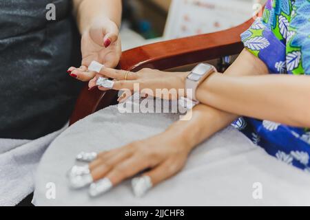 Donna in salone delle unghie che riceve una manicure da un estetista con lana di cotone. Foto Stock