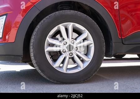Frammento di auto rossa moderna con ruota su disco in acciaio, primo piano. Parte di una nuova vettura gommata moderna con pastiglia del freno a disco. Ruota per auto Red Sports su disco in acciaio Foto Stock