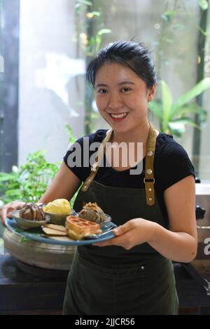 Ragazza vietnamita che serve gelato fatto in casa con waffle in una caffetteria Foto Stock