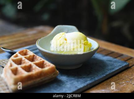 Cucchiaio di gelato biologico al mango in un recipiente in ceramica su un piatto grigio pietra Foto Stock