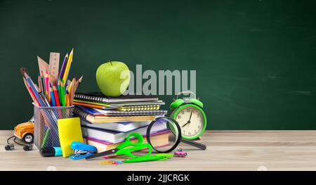 La scuola fornisce composizione con sveglia e mela su tavolo di legno e sfondo verde lavagna. Foto Stock