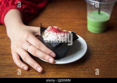 Primo piano torta di ghiaccio e cupcake in un caffè in mani femminili. Foto Stock