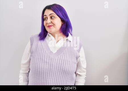 Più taglia donna con capelli viola in piedi su sfondo bianco sorridendo guardando lateralmente e fissando via pensando. Foto Stock