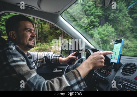 Un uomo che guida un'auto corre in un'area forestale montagnosa. Foto Stock