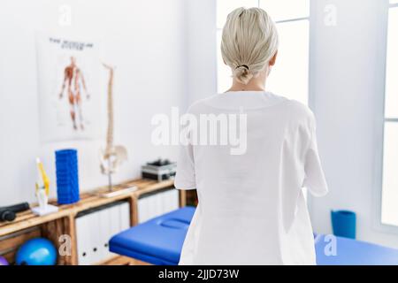 Giovane donna caucasica che lavora alla clinica di recupero del dolore in piedi indietro guardando via con le braccia incrociate Foto Stock