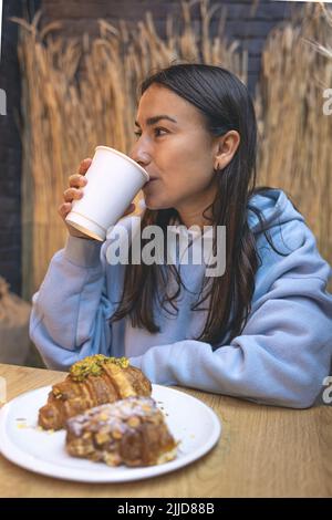 Una giovane donna mangia croissant con caffè in una caffetteria. Foto Stock