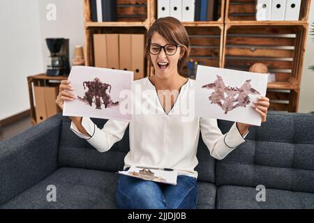 Donna bruna che lavora con rorschach prova alla clinica di psicologia arrabbiato e pazzo urlando frustrato e furioso, urlando di rabbia. Rabbia e aggresssi Foto Stock