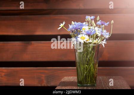 Un bouquet di margherite e fiori di mais in vaso di vetro su un tavolo di legno sullo sfondo di un muro di legno. Luogo per un'iscrizione. Selettivo Foto Stock