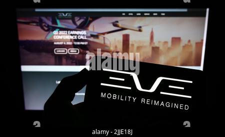 Persona che tiene lo smartphone con il logo della società Eve Holding Inc. (Eve Air Mobility) sullo schermo di fronte al sito Web. Mettere a fuoco sul display del telefono. Foto Stock
