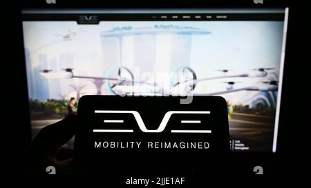 Persona che tiene il telefono cellulare con il logo della società Eve Holding Inc. (Eve Air Mobility) sullo schermo di fronte alla pagina Web. Mettere a fuoco sul display del telefono. Foto Stock