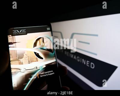 Persona che tiene il cellulare con il sito web della società Eve Holding Inc. (Eve Air Mobility) sullo schermo di fronte al logo. Concentrarsi sul centro del display del telefono. Foto Stock