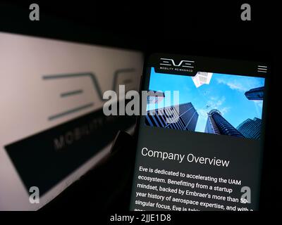 Persona che tiene lo smartphone con la pagina Web della società Eve Holding Inc. (Eve Air Mobility) sullo schermo davanti al logo. Concentrarsi sul centro del display del telefono. Foto Stock