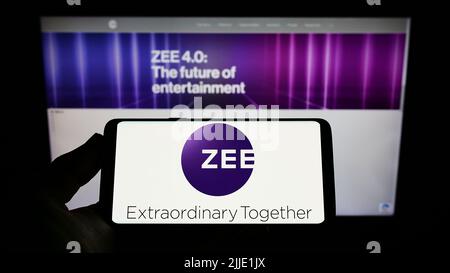 Persona che tiene uno smartphone con il logo della società Zee Entertainment Enterprises Limited sullo schermo di fronte al sito Web. Mettere a fuoco sul display del telefono. Foto Stock