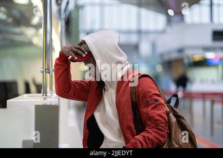 Il triste uomo africano che si trova vicino al banco del check-in si sente frustrato a causa della cancellazione del volo Foto Stock