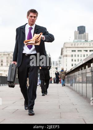 Ora di punta. Un giovane uomo d'affari intelligente che controlla il tempo mentre attraversa London Bridge sulla strada per l'ufficio; da una serie di immagini. Foto Stock