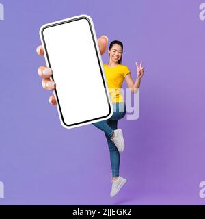 Allegra Signora asiatica che salpano in aria e mostra smartphone Foto Stock