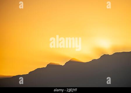 Una bella foto del sole dorato della sera che brilla dietro una montagna Foto Stock