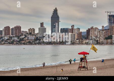 Torre del bagnino con bagnino seduto sotto ombrello e bandiera gialla a Poniente Beach a Benidorm, Alicante, Spagna, Europa Foto Stock