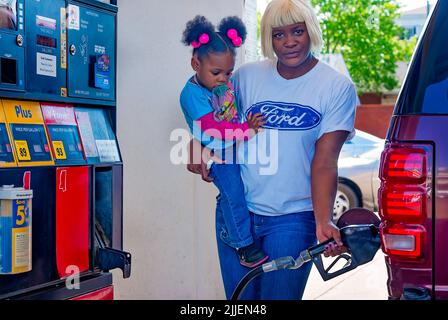 Una donna pompa gas come lei tiene sua figlia, 14 aprile 2011, a Columbus, Mississippi. I prezzi del gas sono aumentati nel 2011 a causa di un indebolimento del dollaro statunitense. Foto Stock