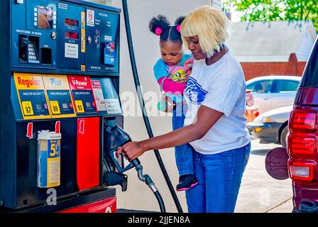 Una donna pompa gas come lei tiene sua figlia, 14 aprile 2011, a Columbus, Mississippi. I prezzi del gas sono aumentati nel 2011 a causa di un indebolimento del dollaro statunitense. Foto Stock