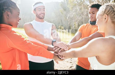 Ci teniamo motivati l'un l'altro. Un gruppo diversificato di amici si trova in piedi insieme con le loro mani accatastate nel mezzo durante il loro allenamento all'aria aperta. Foto Stock