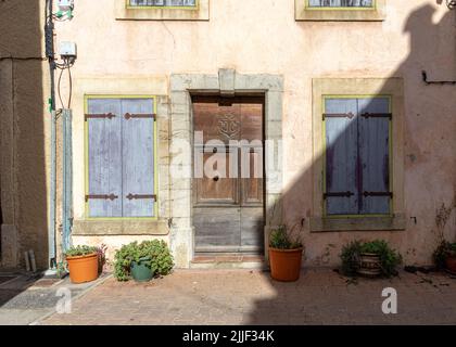 Vecchia casa del villaggio di Gruissan con persiane blu e un attore sulla porta principale in legno, Francia meridionale, con pietra, pareti color beige e blu Foto Stock