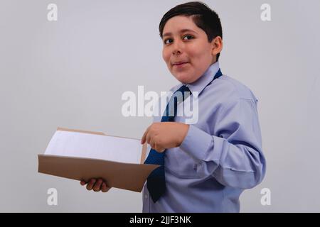 Ragazzo elegantemente vestito da uomo d'affari con una serie di importanti carte. Ragazzo che gioca ad essere un adulto con un vestito e cravatta su uno sfondo bianco isolato mentre tiene una cartella. Foto Stock