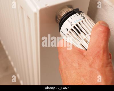 Gira a mano il termostato di un radiatore, risparmia energia, riduci i costi energetici, concetto di riscaldamento Foto Stock