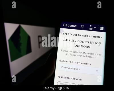 Persona che tiene il cellulare con pagina web della società immobiliare americana Pacaso sullo schermo di fronte al logo. Concentrarsi sul centro del display del telefono. Foto Stock