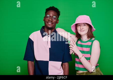 Ritratto di elegante coppia teenage multietnico in abiti di moda sorridenti a macchina fotografica posando su sfondo verde Foto Stock