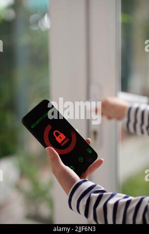 Le mani di una giovane donna che utilizza l'applicazione di controllo della sicurezza sullo smartphone per impostare la sveglia Foto Stock