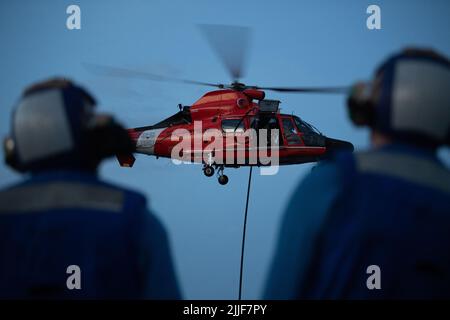 Due membri del Cutter Bear della Guardia Costiera degli Stati Uniti (WMEC 901), guardano verso l'alto un Dolphin MH-65 della Guardia Costiera, un bene della Guardia Costiera Helicopter Interdiction Tactical Squadron (HITRON), durante le esercitazioni di qualificazione di atterraggio del ponte, Oceano Atlantico, 13 luglio 2022. Le qualifiche per l'atterraggio sul ponte consentono sia all'equipaggio di bordo che all'equipaggio di addestrare con successo il personale per l'atterraggio di un elicottero a bordo di una nave. (STATI UNITI Foto della Guardia Costiera di Petty ufficiale 3rd Classe Matthew Abban Foto Stock