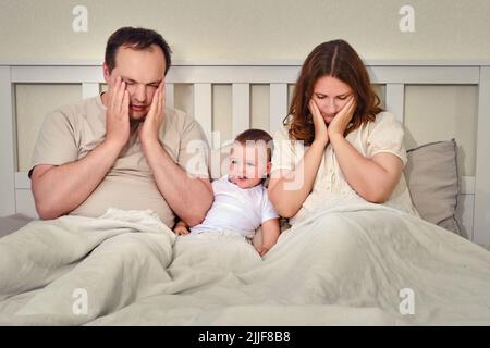 Una donna e un uomo sono in dubbio dopo la nascita di un bambino piccolo sul letto. Padre e madre con un bambino, genitori premurosi e un bambino Foto Stock