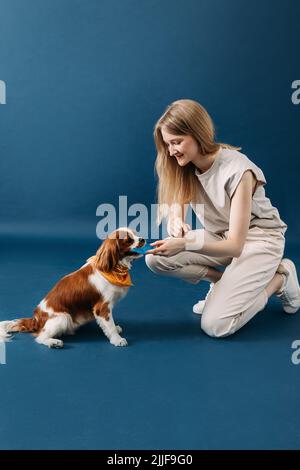 Vista laterale della giovane donna che gioca con il suo cane su sfondo blu Foto Stock
