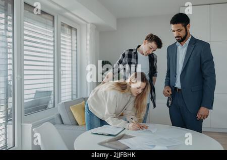 Giovane coppia firma contratto quando acquistare la loro nuova casa e ricevere chiavi da agente immobiliare. Foto Stock