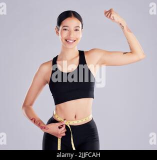 Tonificare è l'obiettivo. Una giovane donna attraente in piedi in studio e utilizzando un nastro di misurazione intorno alla sua vita. Foto Stock