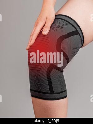 Donna che indossa un sostegno per le ginocchia per ridurre il dolore o prevenire lesioni durante lo sport. Gamba femmina con punto rosso. Legamenti irrorati, rotti, lacrima menisco, tendinite, artrite. Foto di alta qualità Foto Stock