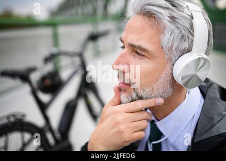 Uomo d'affari con bicicletta seduta su panca, ascolto di musica e riposo. Concetto di pendolarismo e trasporto alternativo Foto Stock