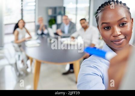 Presentare un altro piano vincente a tutti. Una giovane donna d'affari che scrive appunti mentre presenta una presentazione ai suoi colleghi in ufficio. Foto Stock