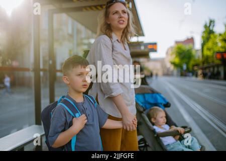 Giovane madre con bambini in attesa sulla fermata dell'autobus in città. Foto Stock