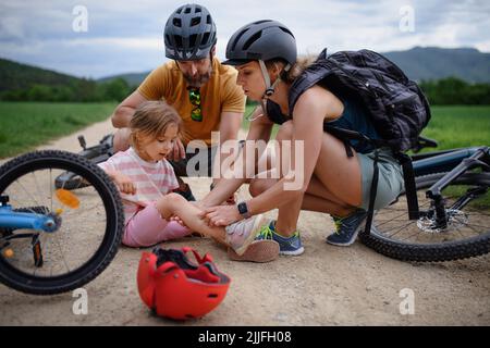 Madre e padre che aiutano la loro bambina dopo essere caduta fuori della bicicletta all'aperto Foto Stock