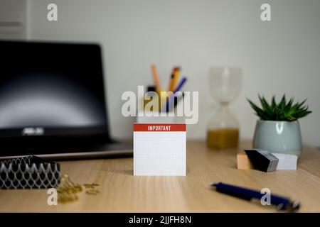 Un blocco note per note importanti su una scrivania caotico con un computer portatile Foto Stock