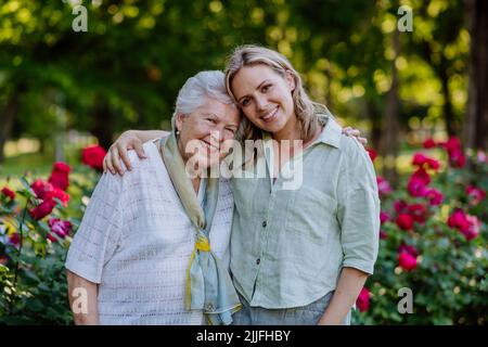 Ritratto di nipote adulto con nonna anziana a piedi nel parco, con rose sullo sfondo Foto Stock