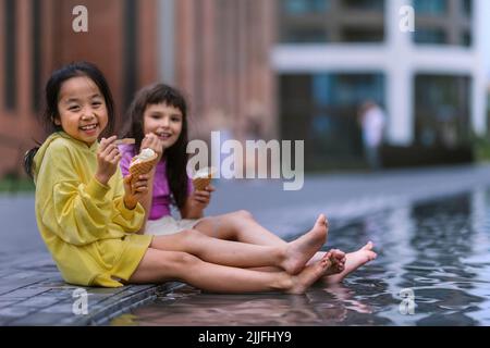 Due ragazze sedute, con gambe in fontana, gelato e giorno d'estate. Foto Stock