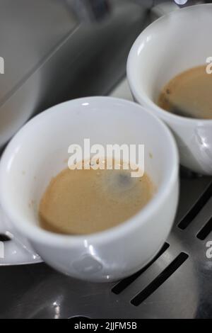 Espresso appena fatto con crema in schiuma appena preparata in tazze da caffè in ceramica. Preparazione del caffè mattutino a casa. Foto Stock